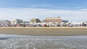 Une plage avec des parasols et des chaises longues, un rivage sablonneux et des bâtiments en arrière-plan.