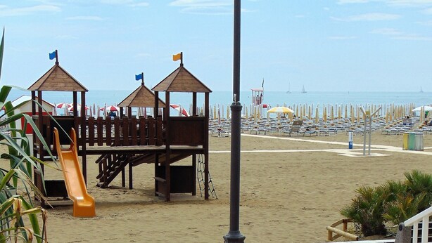 Une terrasse au bord de la plage, dotée de meubles en osier, d’un espace de jeux pour enfants et offrant une vue sur la plage.