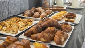 Une table de buffet proposant diverses pâtisseries et du pain, un distributeur de café et un panier de fruits.