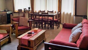 A cozy living room with a wooden ceiling, a dining area with a table and chairs, and a red sofa. - Alquimia Cabañas Apart (El Bolson)
