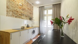 Una cocina moderna con pared de ladrillo, lavadora y mesa de comedor con un florero.