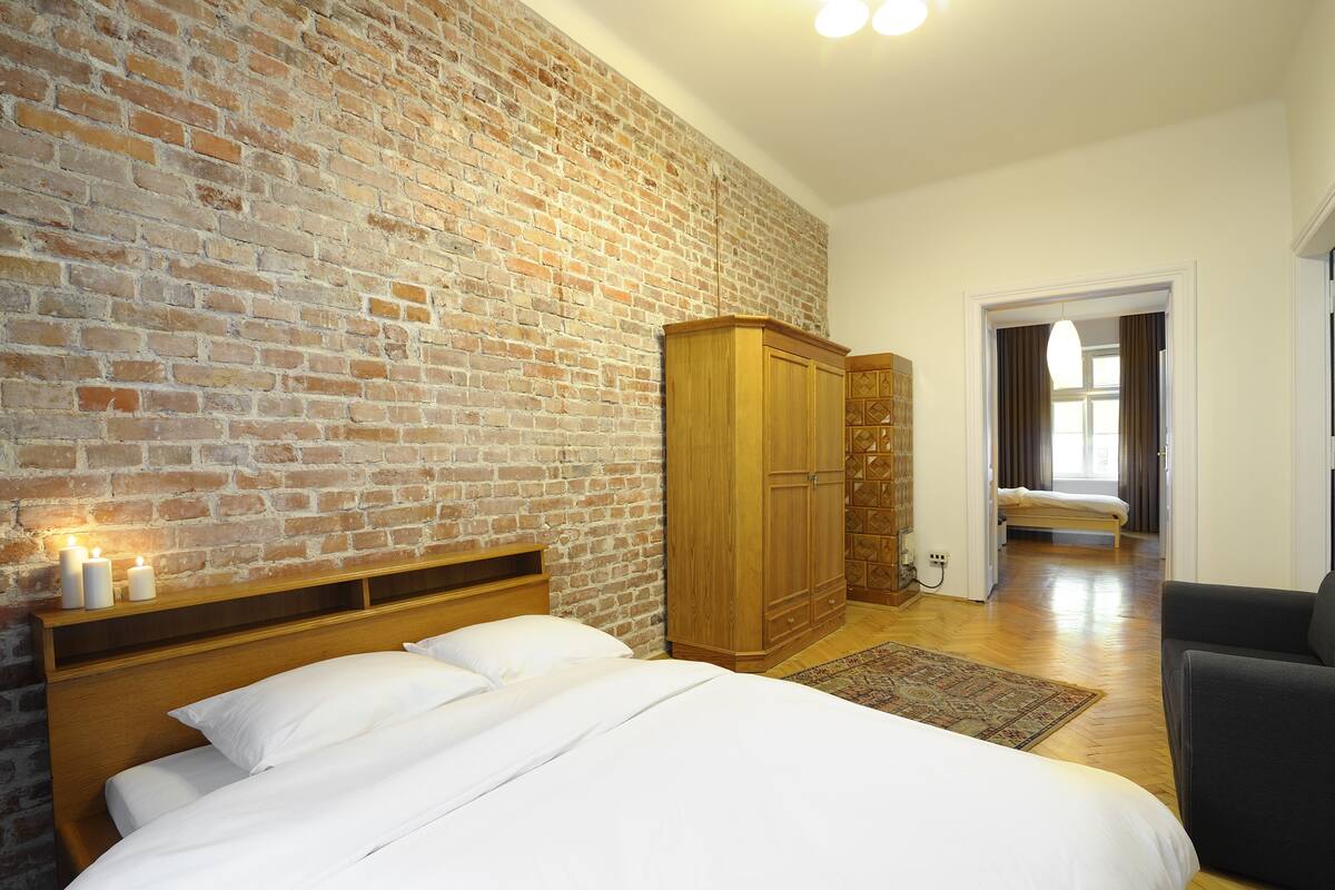 A bedroom with a brick wall, wooden headboard, a wardrobe, and a bed with white linens.