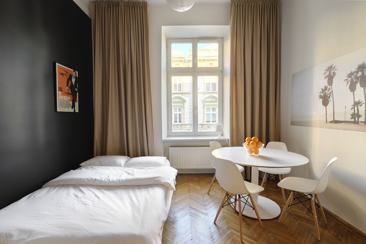 A bedroom with a bed, a window, a table with chairs, and a painting on the wall.