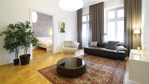 Una sala moderna con un sofá, un sillón y una mesa de centro. Se ve una planta en maceta, una alfombra y una pared de ladrillo.