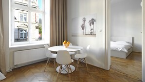 Una habitación con una mesa de comedor y sillas, una cama, un radiador y una ventana con cortinas.