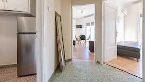 A hallway with a stainless steel refrigerator, a wooden-framed mirror leaning against the wall, and a dining area with a table and chairs.