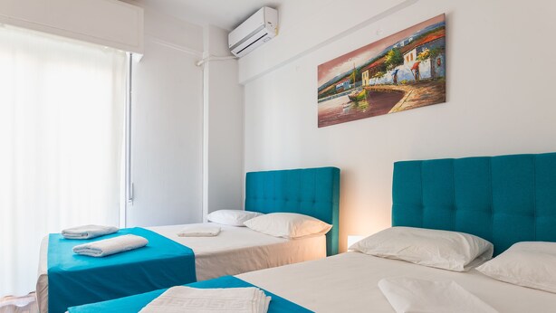 A hotel room with two beds, each with a blue bedspread and white pillows. There is a painting on the wall depicting a coastal scene.