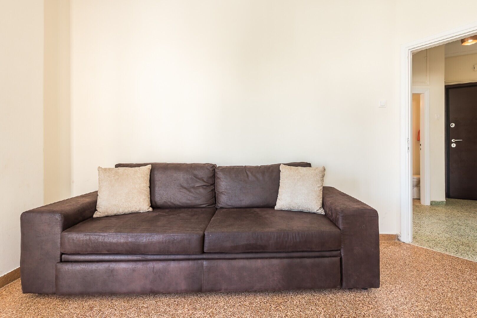 A dark brown leather sofa with three cushions in a room with white walls and a carpeted floor.