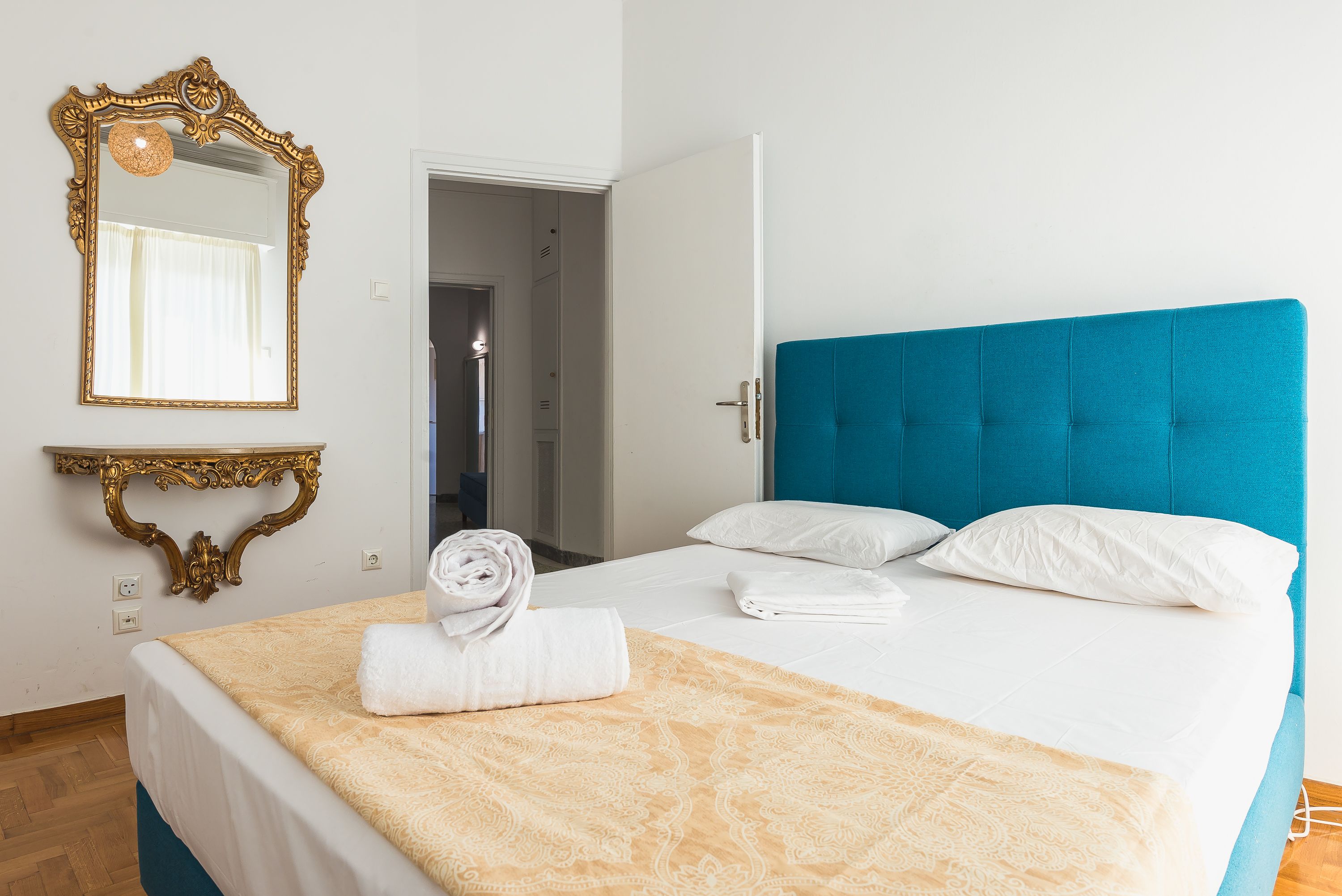 A neatly made bed with a blue headboard, a gold-framed mirror, and a folded towel on the bed.