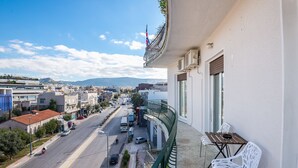 A balcony with a view of a city street, a table, and chairs.