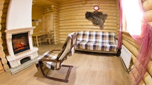 A log cabin interior with a fireplace, a checkered sofa, and a wooden rocking chair. - Baza otdikha Zhuravushka (Sosnovskoye)