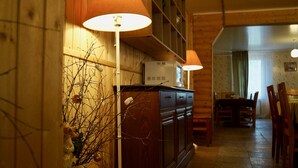 A wooden interior with a kitchen area, including cabinets, a refrigerator, and a dining table with chairs. - Baza otdikha Zhuravushka (Sosnovskoye)
