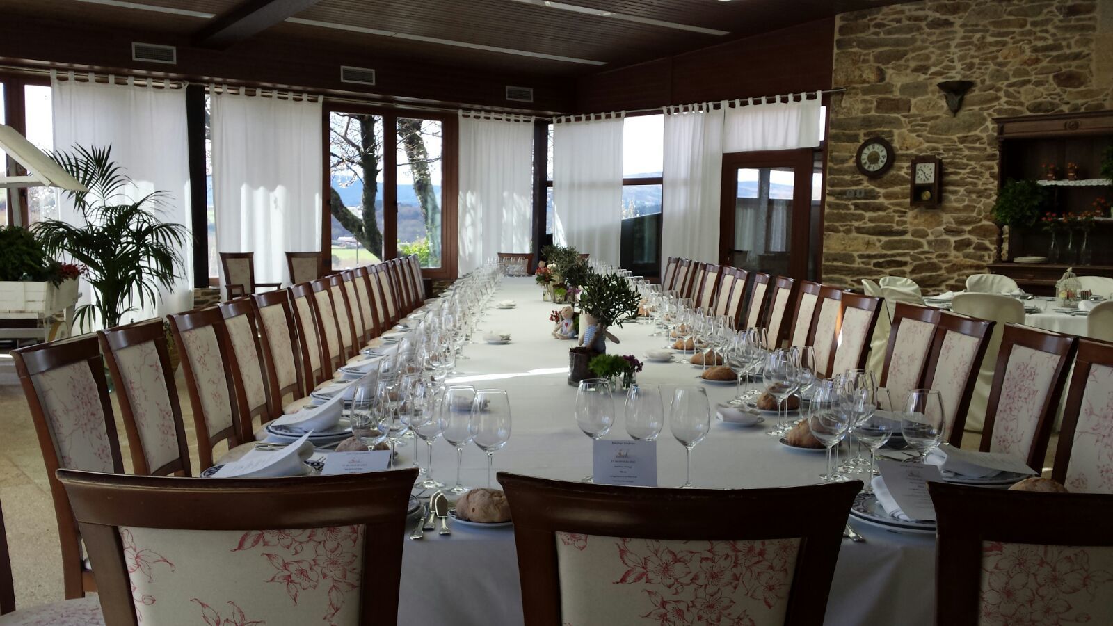 Una larga mesa de comedor dispuesta para una comida formal, con sillas, copas de vino y platos.