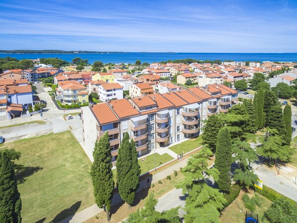 A residential area with multi-story buildings, a clear view of the sea, and a well-maintained green space.