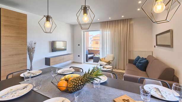 Un comedor moderno con una mesa dispuesta para cuatro, un frutero y un sofá al fondo.