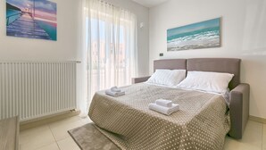 Un dormitorio con cama, una ventana con cortinas, un radiador y dos cuadros en la pared.