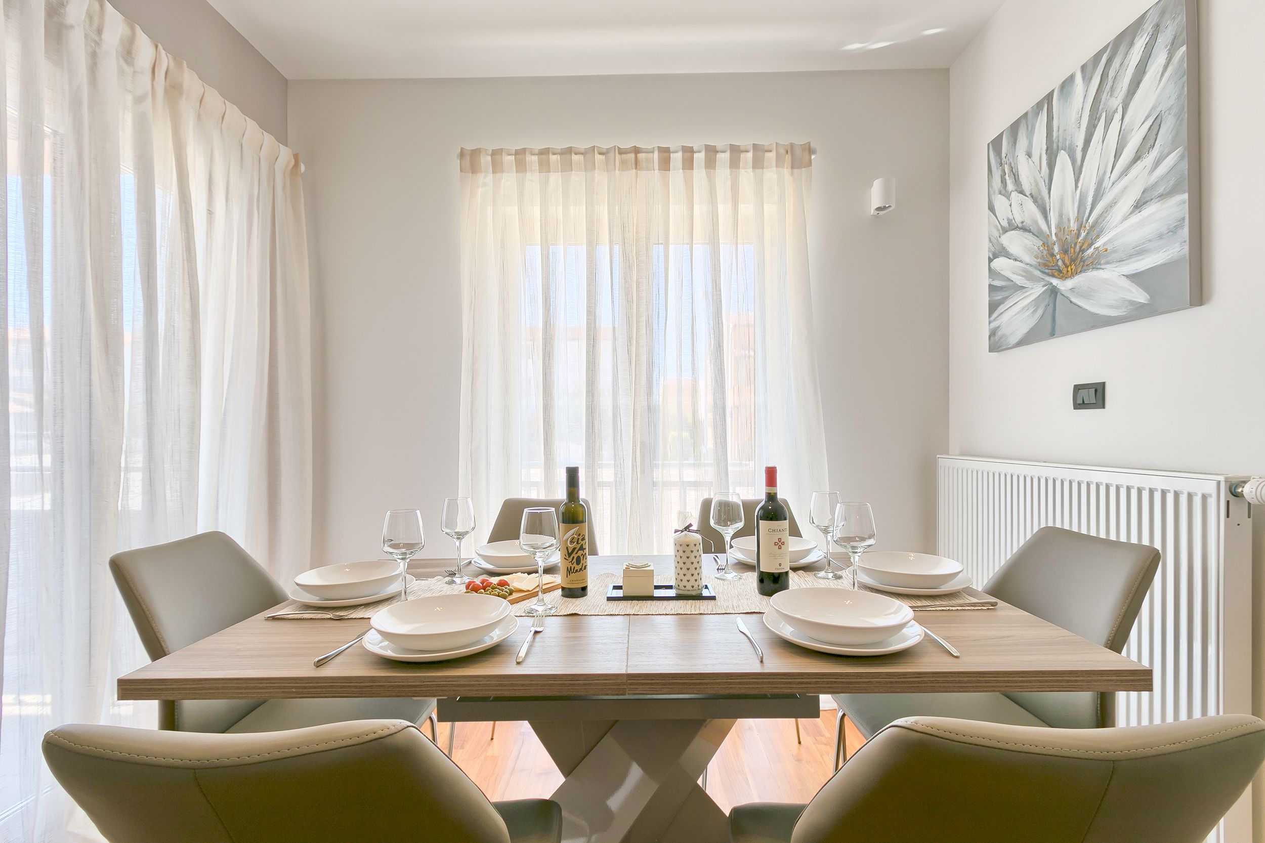 A dining room with a wooden table set for four, white plates, wine glasses, and a bottle of wine.