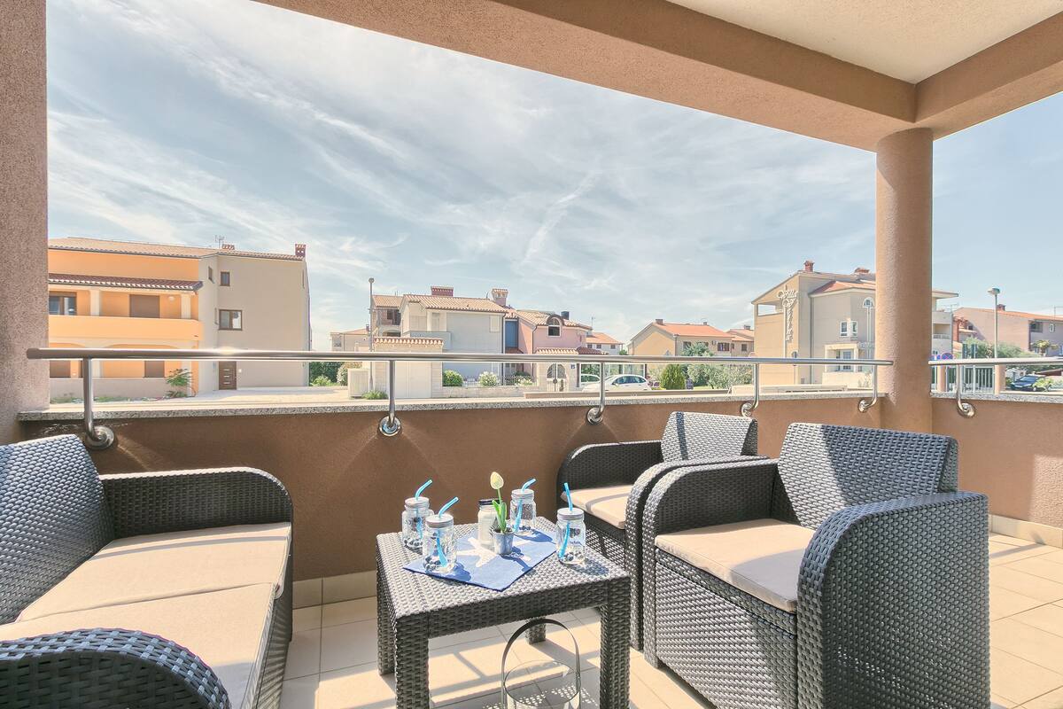 Ein Balkon mit Korbmöbeln und einem Tisch, gedeckt mit Getränken und einer Blume.
