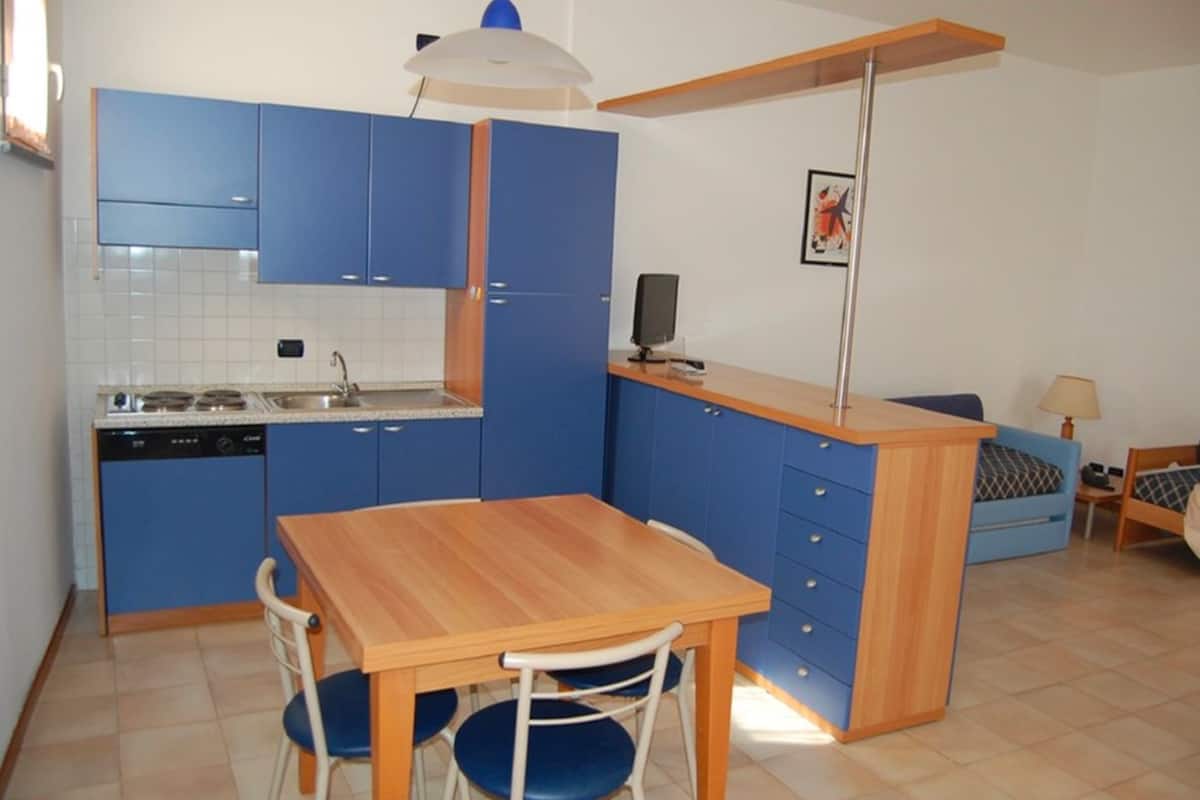 A compact kitchen with blue cabinets, a wooden dining table, and a small island with a sink.