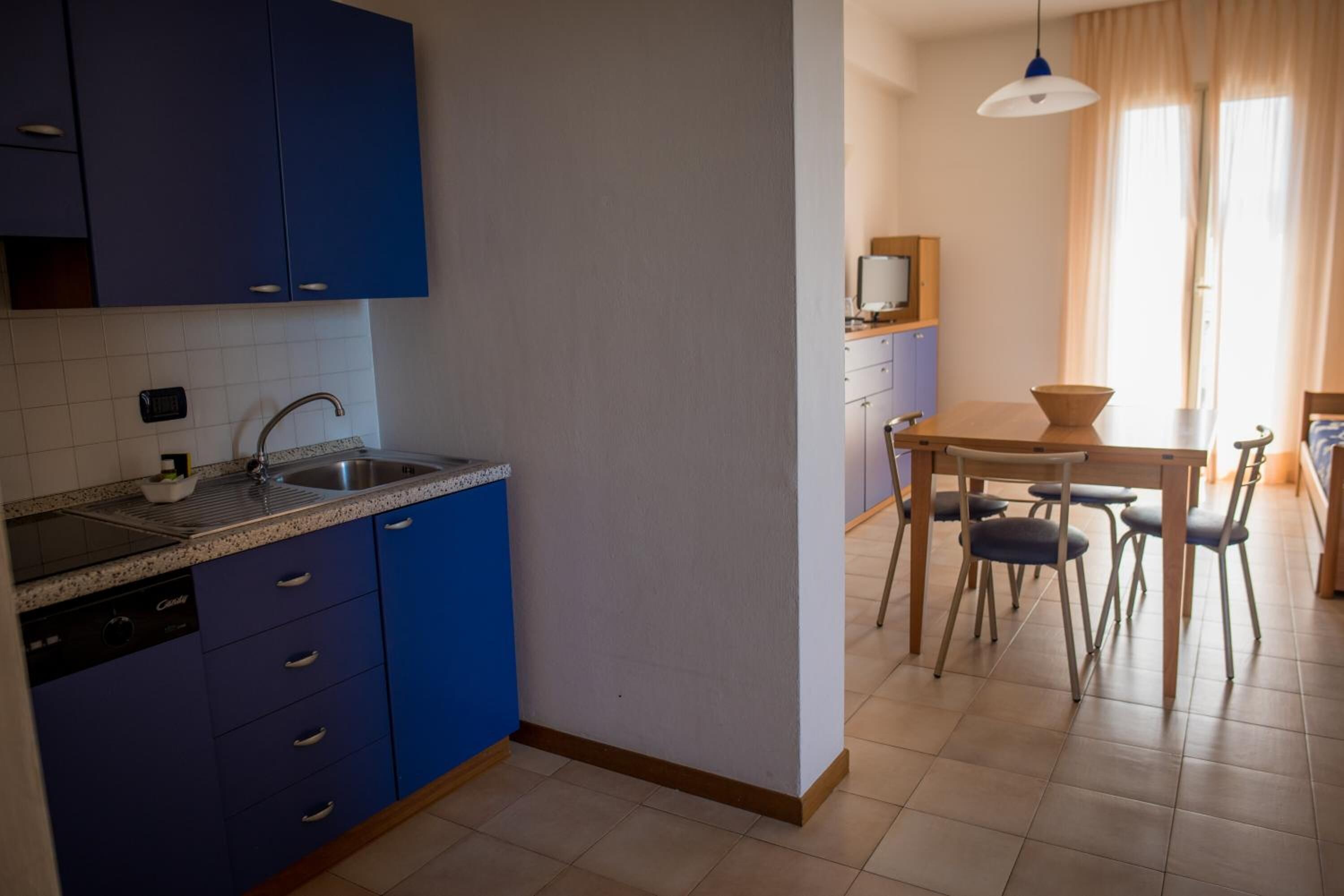 Une cuisine avec des meubles de couleur bleue, un lave-vaisselle et un évier. On y trouve également un coin repas avec une table et des chaises.