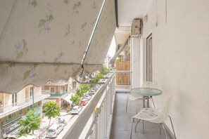 A balcony with a glass table and chairs, overlooking a street with parked cars and buildings. - Victoria Best Apartments (Athens)