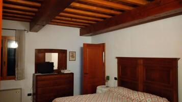 Quarto com teto de madeira, cama com colcha estampada, cômoda, espelho e porta.