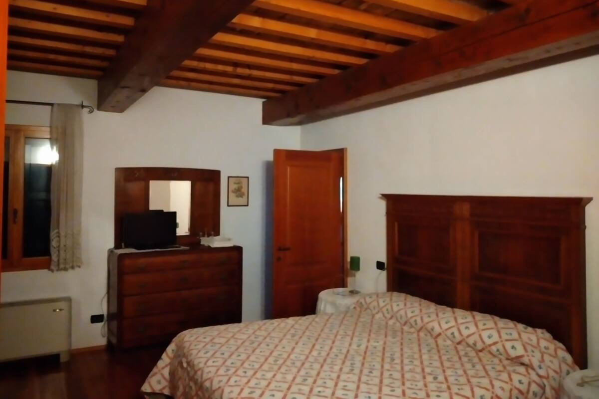 Une chambre avec un plafond en bois, un lit recouvert d’une couvre-lit à motifs, une commode, un miroir et une porte.