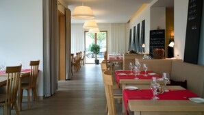 A restaurant with wooden tables and chairs, red tablecloths, and hanging pendant lights. - WeinKulturgut Longen-Schlöder (Longuich)