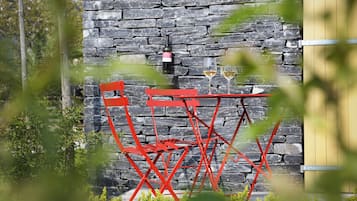 Un muro de piedra con una mesa y sillas de metal rojo, y dos copas de vino sobre la pared.
