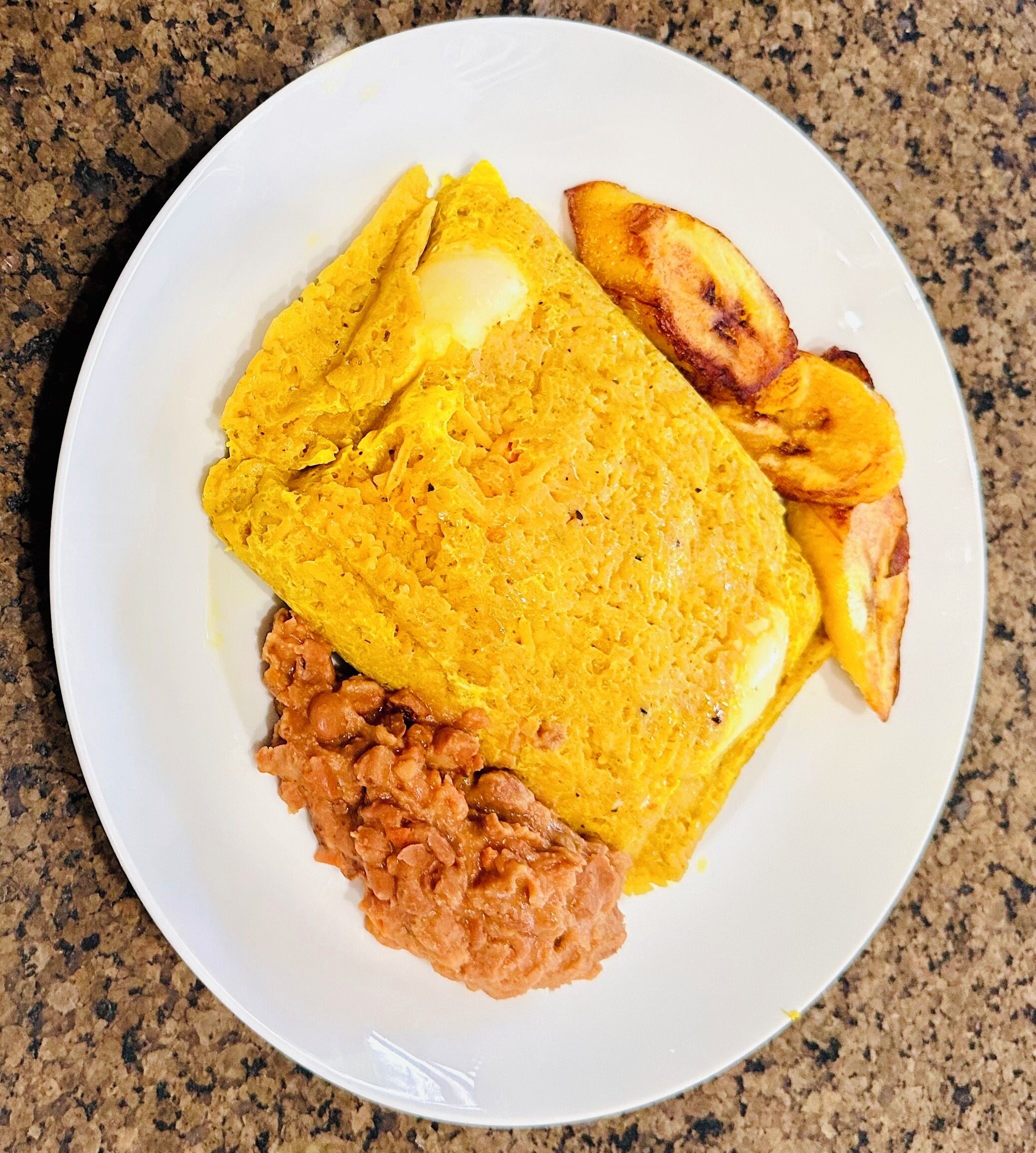 A plate with an omelette, fried plantains, and beans.
