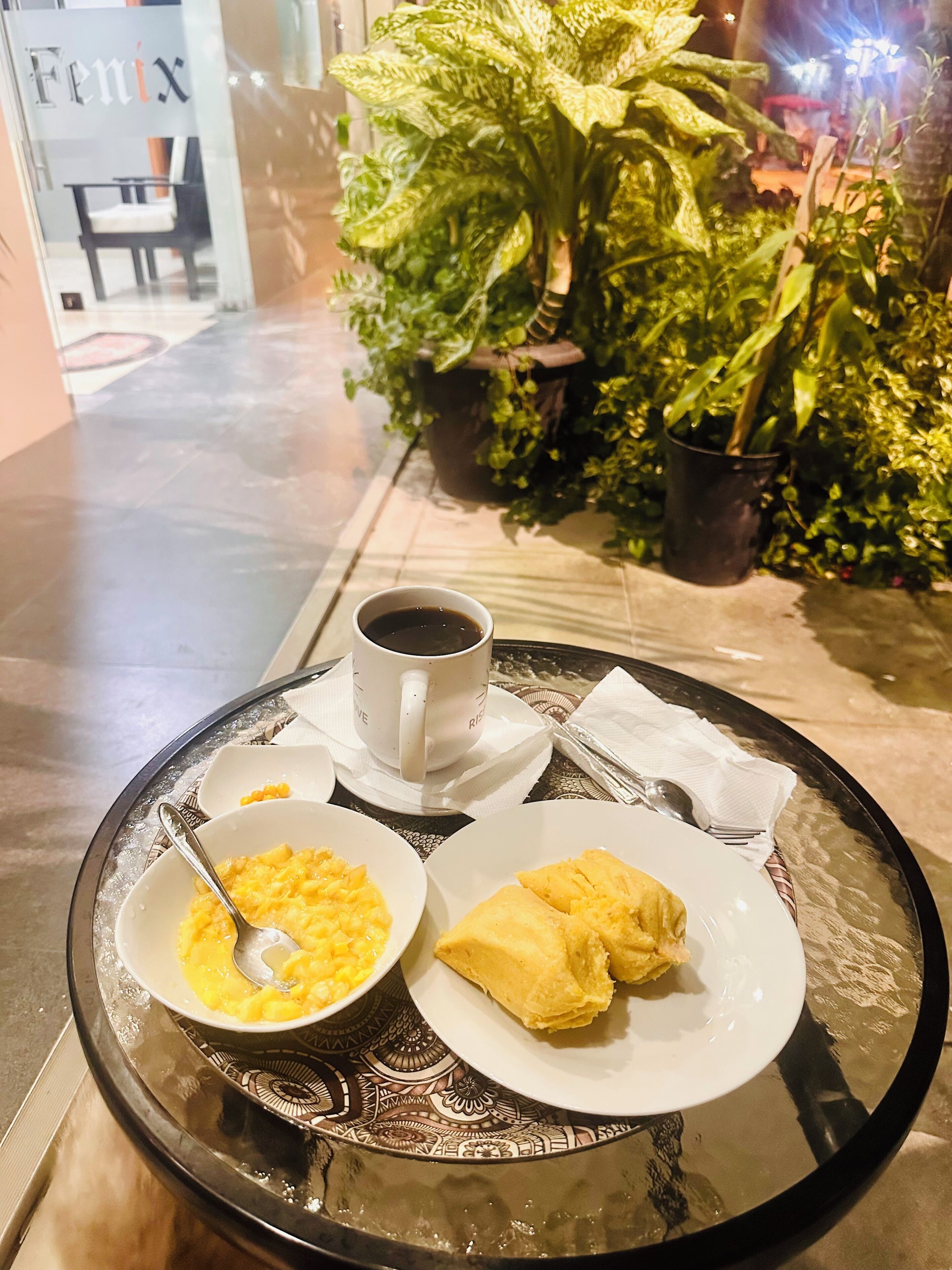 Een dienblad met een kop koffie, een kom roerei en een bord gebakjes op een glazen tafel.