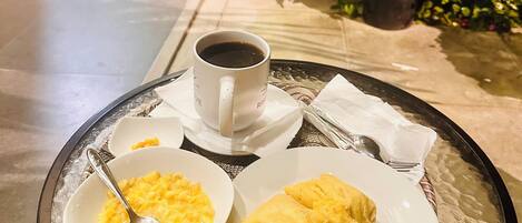 Un plateau avec une tasse de café, un bol d’œufs brouillés et une assiette de viennoiseries sur une table en verre.