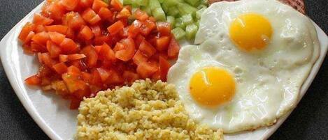 A plate with two fried eggs, diced tomatoes, diced cucumbers, and a portion of couscous.