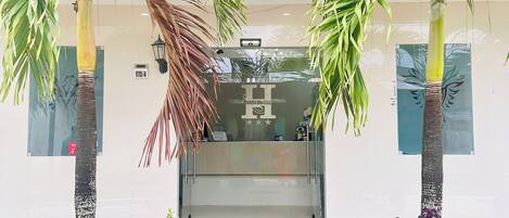 A hotel entrance with a glass door, palm trees, and a variety of plants.