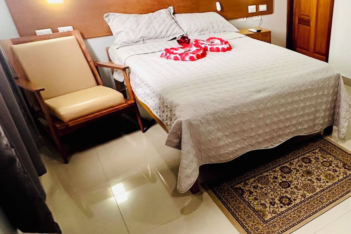 A neatly arranged hotel room with a bed, a chair, a nightstand, and a wooden door.