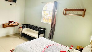 A bedroom with a bed, a chair, a small table, an air conditioner, and a window with curtains. - Hotel Fenix (Iquitos)