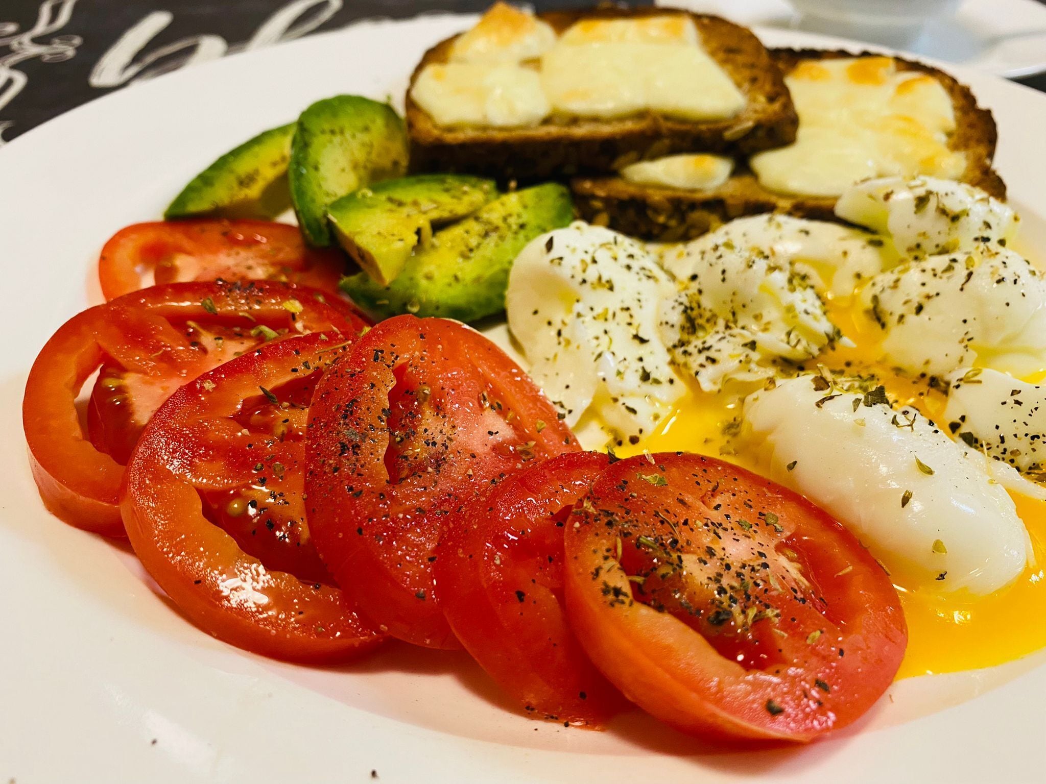 A plate with sliced tomatoes, avocado, and poached eggs.