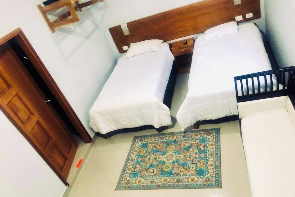 A room with two beds, a wooden headboard, a patterned rug, and a white sofa.