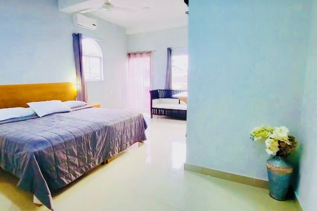 A bedroom with a bed, a nightstand, a chair, and a vase of flowers.