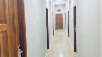A corridor with a wooden door on the left, a tiled floor, and a door at the end with a sign above it.