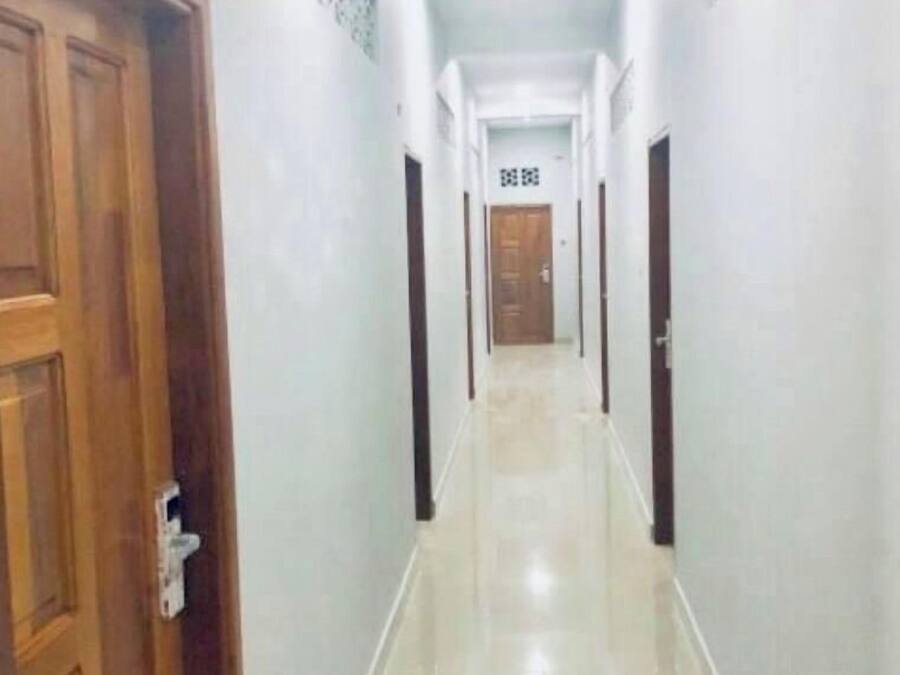 A corridor with a wooden door on the left, a tiled floor, and a door at the end with a sign above it.