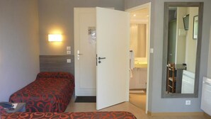A hotel room with two beds, a door leading to a bathroom, and a mirror on the wall.