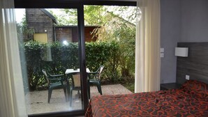 A bedroom with a bed, a window with curtains, and a view of an outdoor area with a table and chairs.