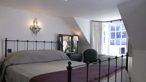 A bedroom with a bed, a nightstand, a mirror, a lamp, and a window with curtains. - Melville House (Crieff)