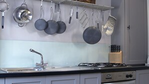 A kitchen with grey cabinets, a gas stove, a sink, hanging pots, and a fish display on the wall. - Melville House (Crieff)