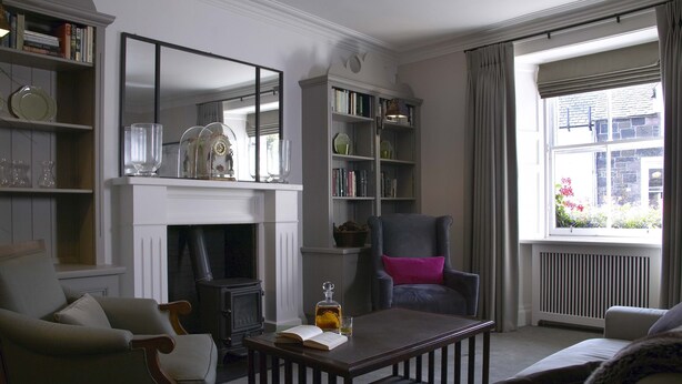 A living room with a fireplace, bookshelves, a coffee table with a book and a bottle, and a window with curtains. - Melville House (Crieff)