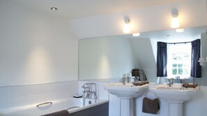 A modern bathroom with a bathtub, two sinks, and a large mirror. - Melville House (Crieff)