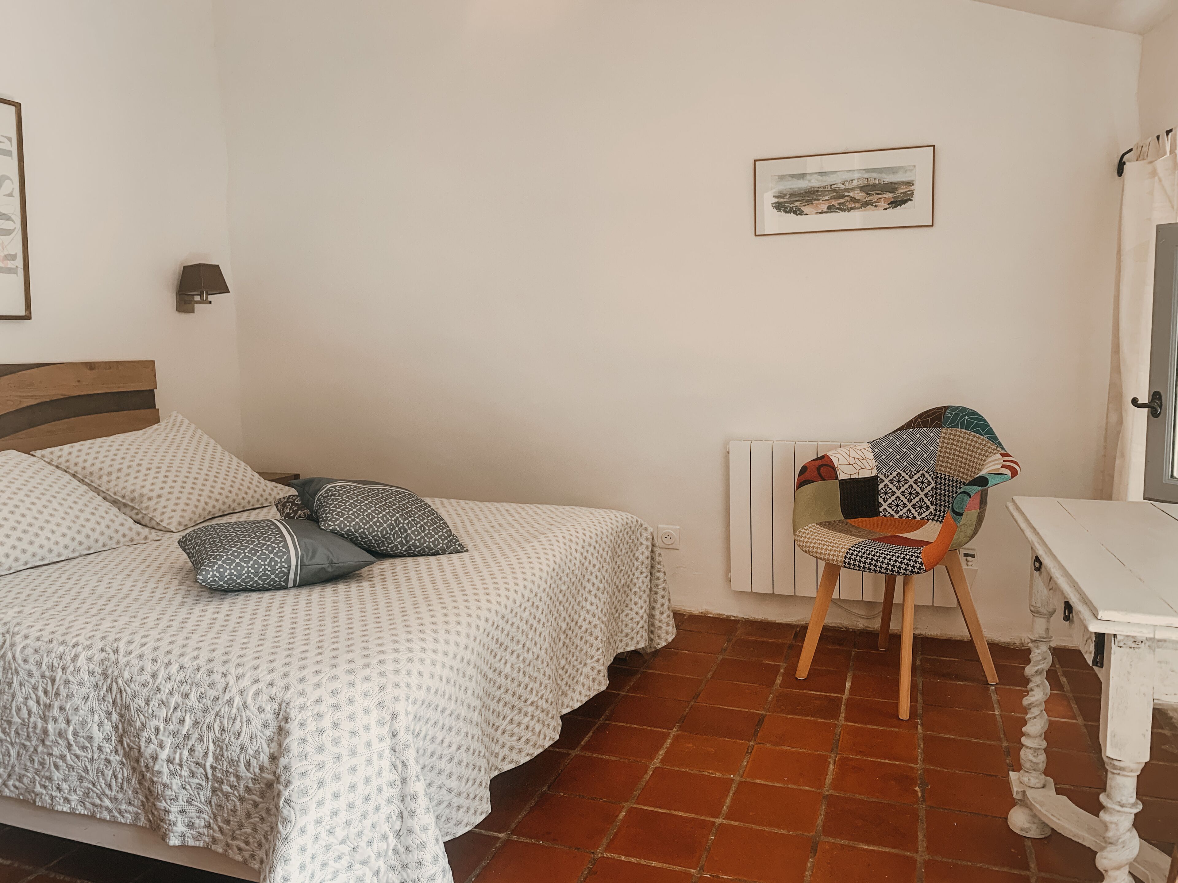 Un dormitorio con una cama, una silla, un radiador y un cuadro en la pared.