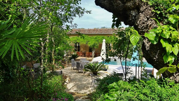 A lush garden with a pool, outdoor seating, and a building with a tiled roof. - Mas Escombelle Chambre d'Hôte (Barjac)