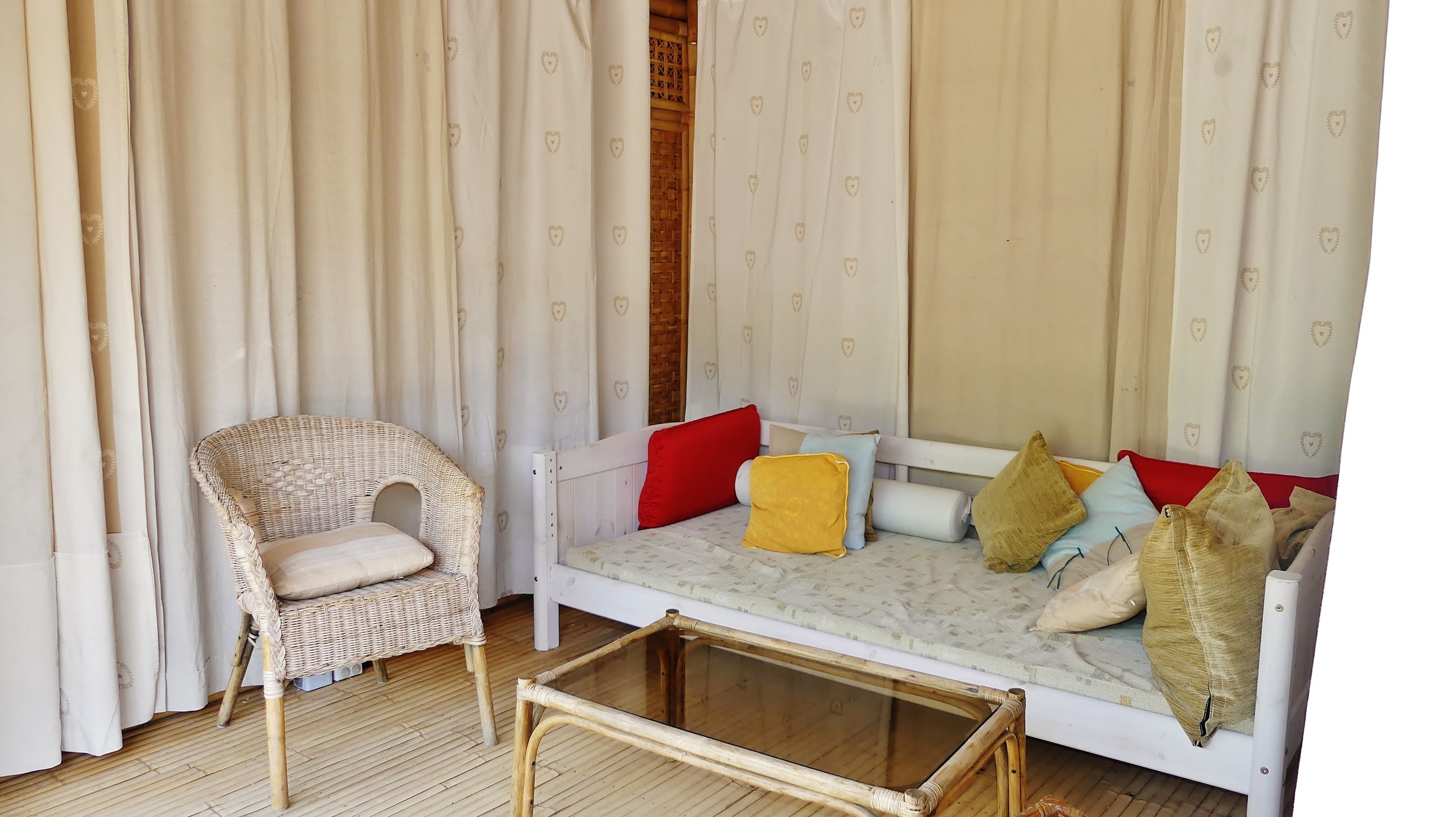 A room with a wicker chair, a white sofa with colorful cushions, and a glass-top coffee table.